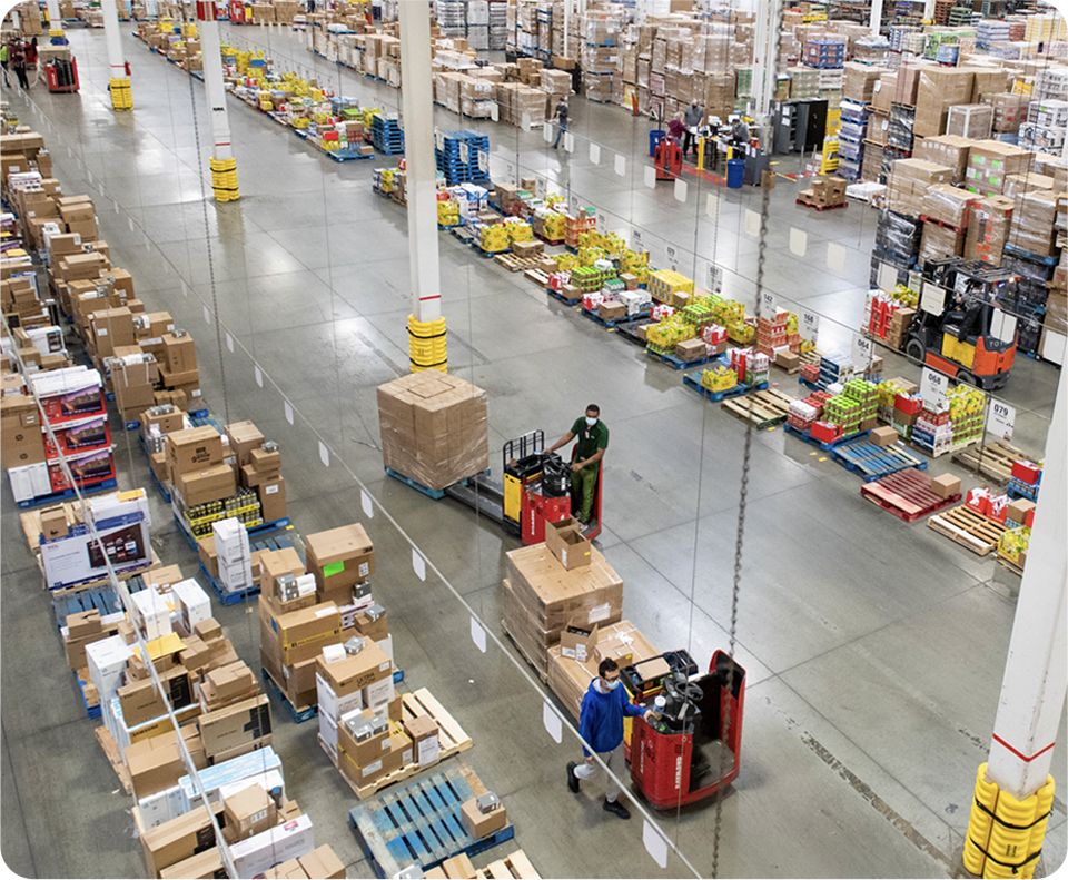 Image: Aerial view of a busy warehouse with workers handling packages and operating forklifts.
