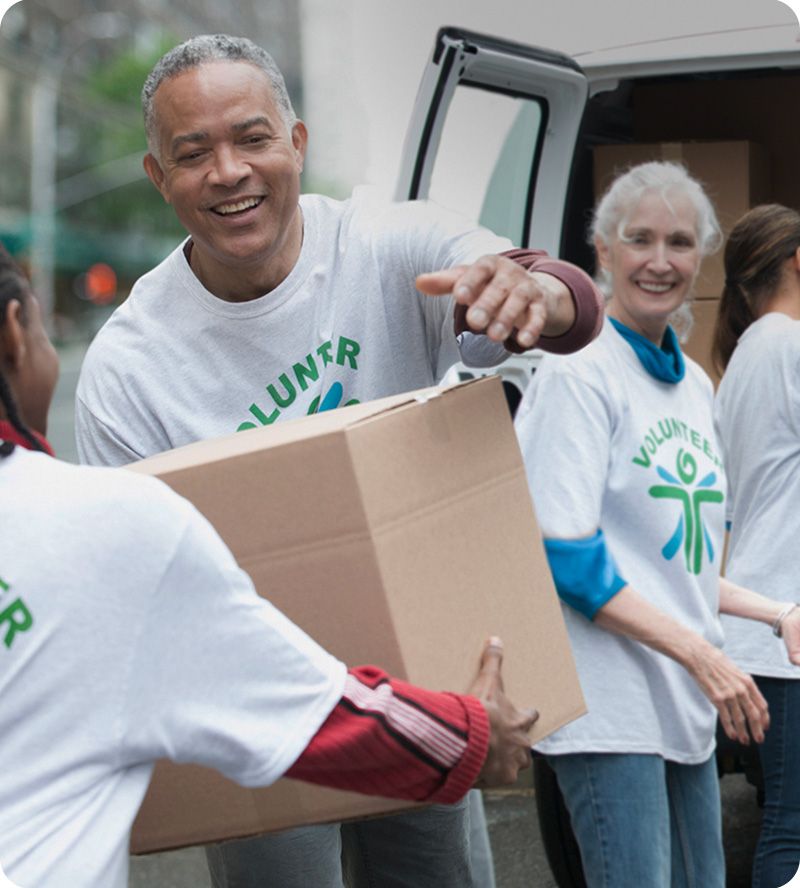 Image: Group of volunteers wearing matching T-shirts, with one man handing a box to another person.