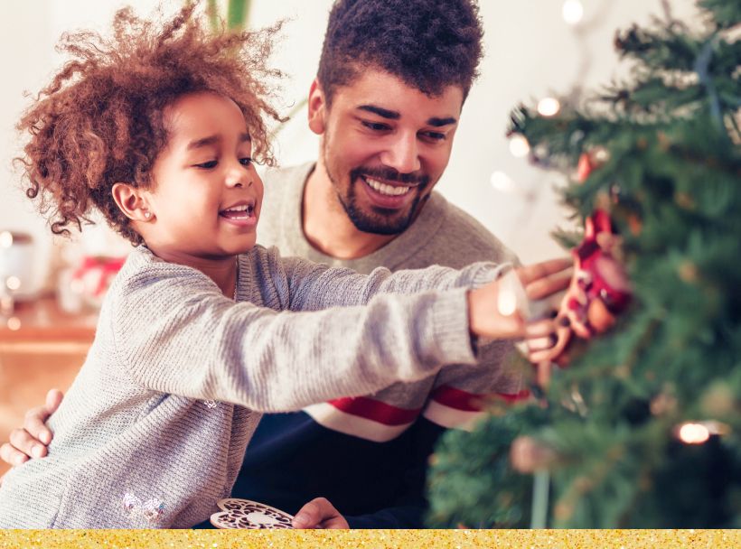 Image: Father and child smiling, and decorating a Christmas tree.