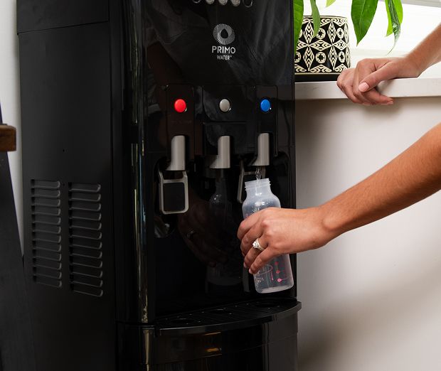 Woman drinking water next to a water dispenser