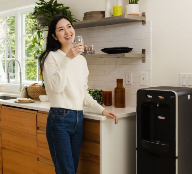 Woman drinking water next to a water dispenser