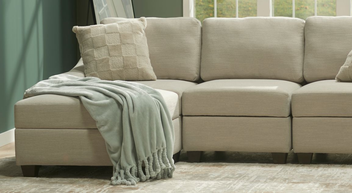 A beige, L-shaped sectional with a pillow and cozy blanket draped over the corner