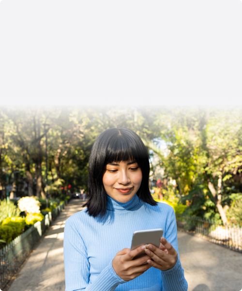 A potential customer checking her phone while walking down a gravel path through the park
